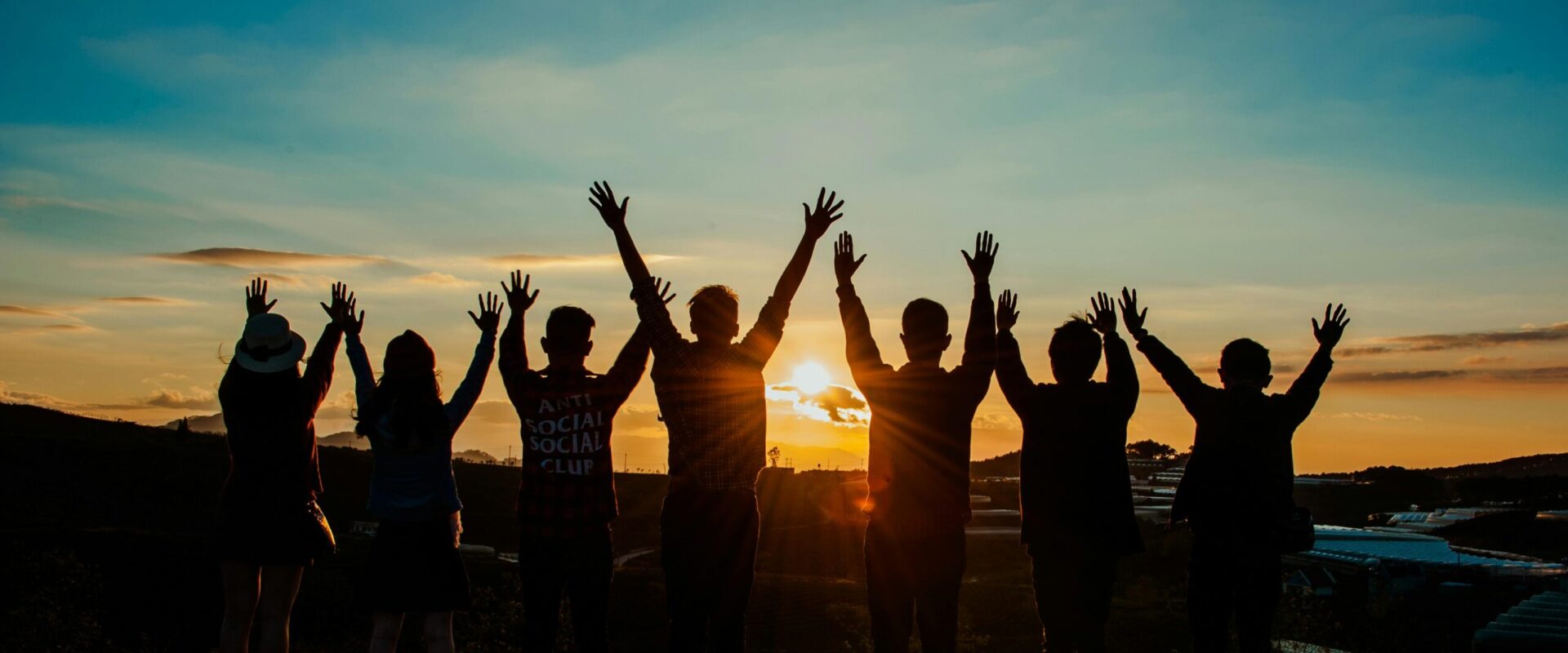 A diverse group of friends raises their arms in celebration against a vibrant sunset backdrop.