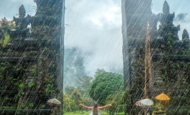 Woman in vibrant rain at iconic Handara Gate, Bali. A magical travel moment.