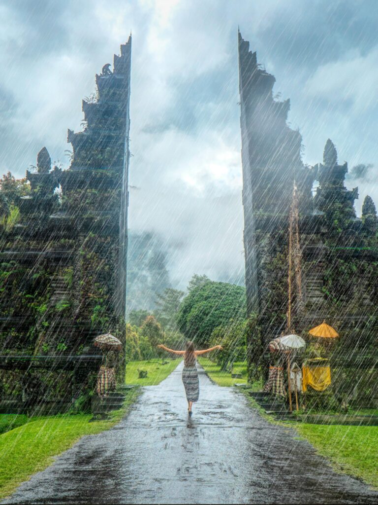 Woman in vibrant rain at iconic Handara Gate, Bali. A magical travel moment.