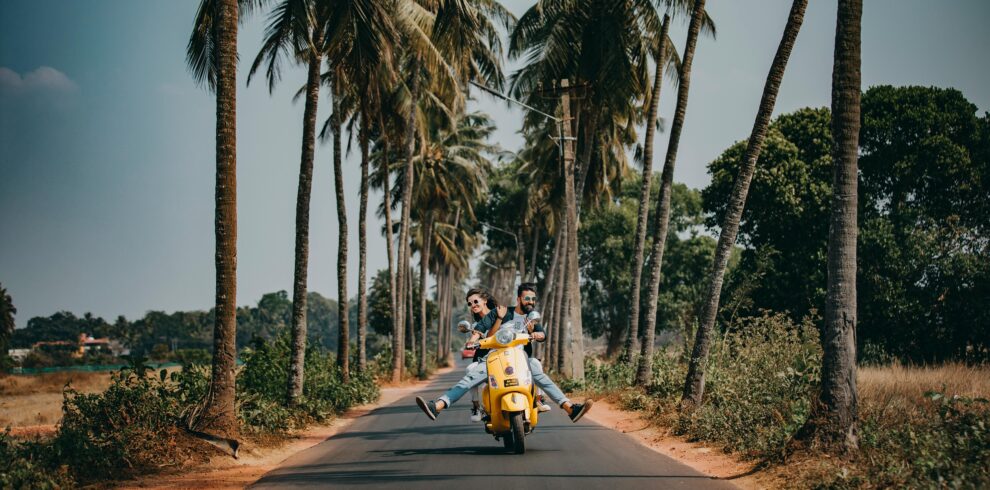 A joyful couple rides a yellow scooter through a scenic palm-lined road, capturing the essence of tropical travel and adventure.
