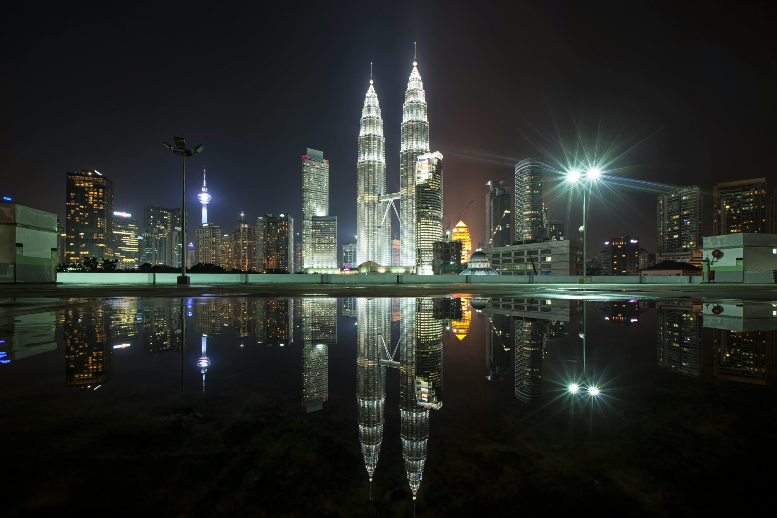 Beautiful view of Kuala Lumpur's skyline featuring the iconic Petronas Towers at night with city lights and reflections.