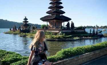 A woman enjoying the serene view of Ulun Danu Beratan Temple by the lake in sunny Bali, Indonesia.