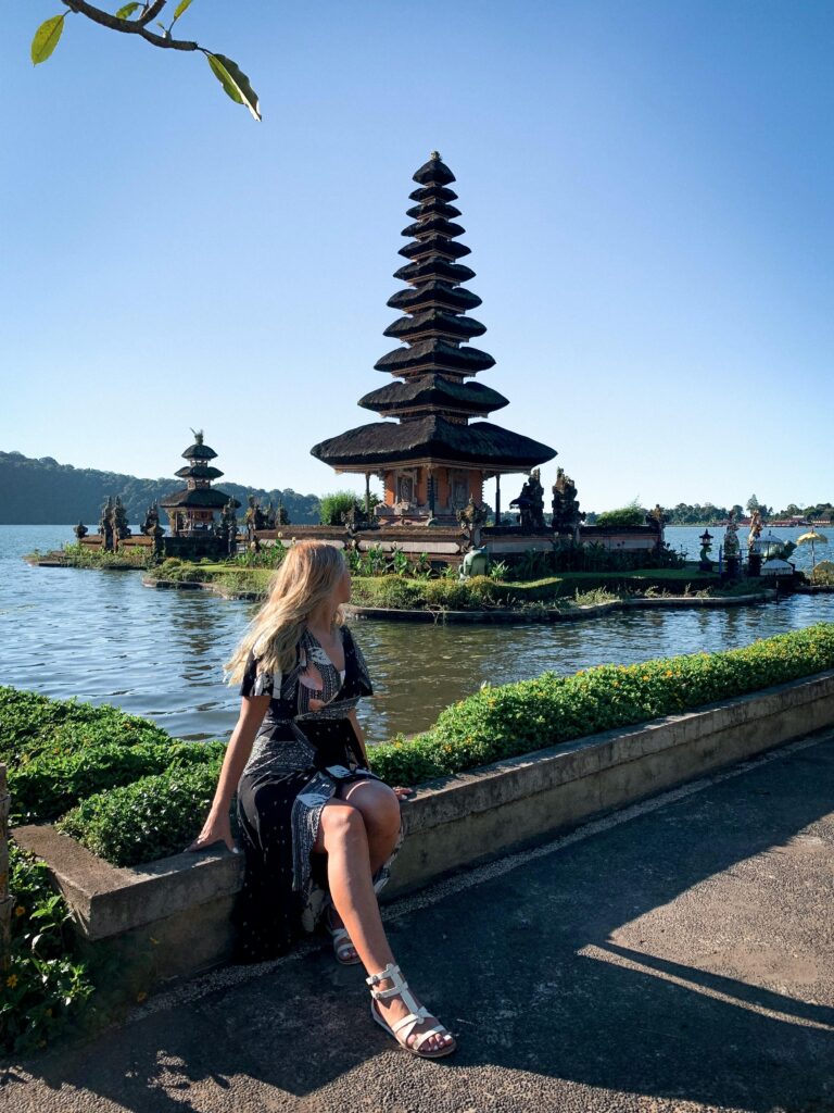 A woman enjoying the serene view of Ulun Danu Beratan Temple by the lake in sunny Bali, Indonesia.