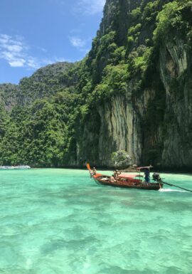 Scenic view of a traditional Thai longtail boat on emerald waters with lush limestone cliffs in Thailand.