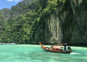 Scenic view of a traditional Thai longtail boat on emerald waters with lush limestone cliffs in Thailand.