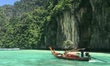 Scenic view of a traditional Thai longtail boat on emerald waters with lush limestone cliffs in Thailand.
