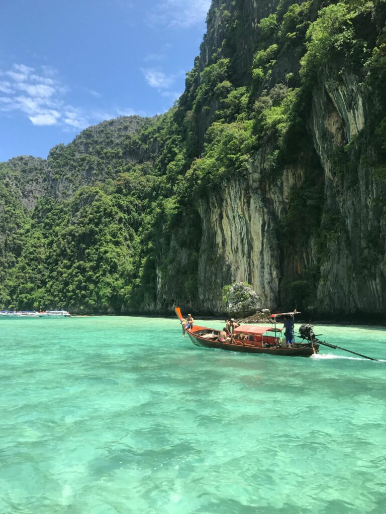 Scenic view of a traditional Thai longtail boat on emerald waters with lush limestone cliffs in Thailand.