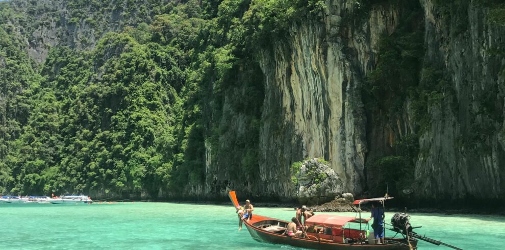 Scenic view of a traditional Thai longtail boat on emerald waters with lush limestone cliffs in Thailand.