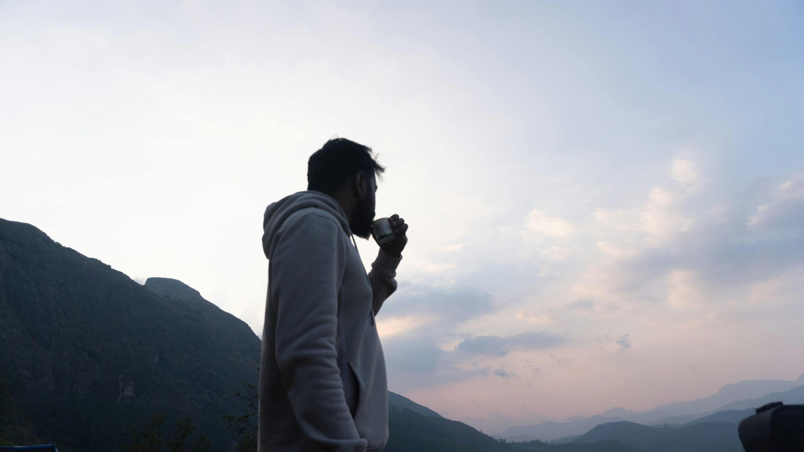 A man drinks coffee while enjoying a stunning view of the mountains in Munnar, Kerala.