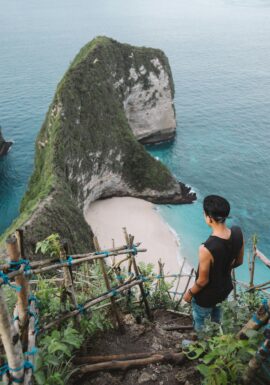 Man overlooks stunning Kelingking Beach from a cliff, Bali's iconic paradise with turquoise waters.