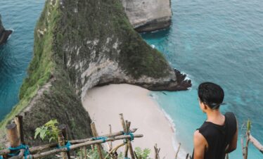 Man overlooks stunning Kelingking Beach from a cliff, Bali's iconic paradise with turquoise waters.