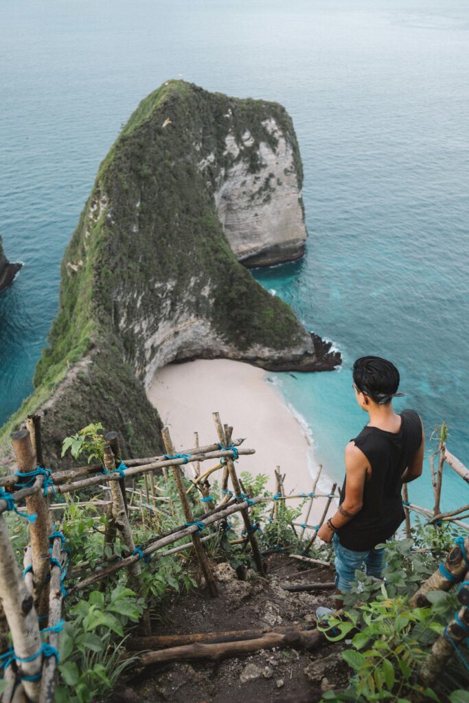 Man overlooks stunning Kelingking Beach from a cliff, Bali's iconic paradise with turquoise waters.
