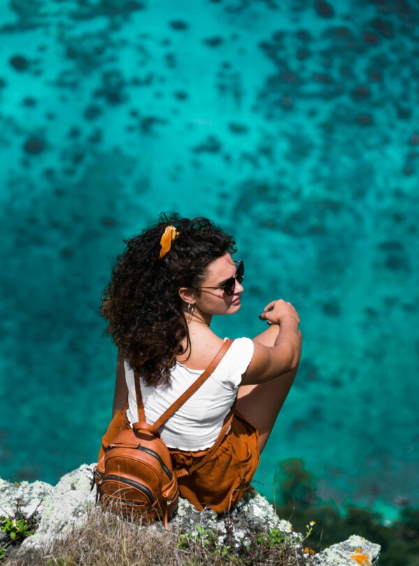 A woman sits on a cliff with a stunning view of the clear turquoise ocean below.