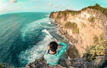 Man sitting on a cliff edge enjoying the ocean view in Bali. Perfect for travel and relaxation themes.