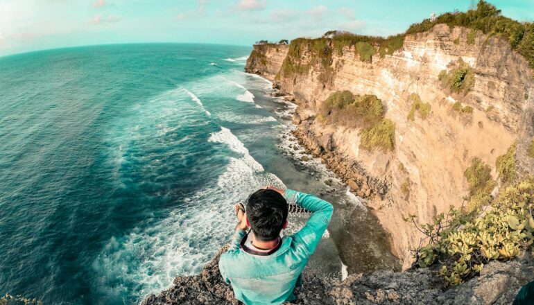 Man sitting on a cliff edge enjoying the ocean view in Bali. Perfect for travel and relaxation themes.