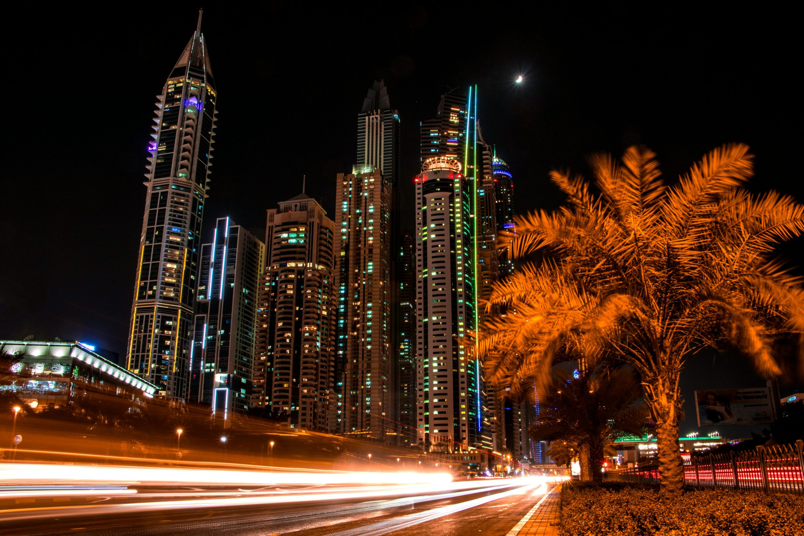 Stunning night view of Dubai's illuminated skyscrapers and palm trees with light trails from passing cars.
