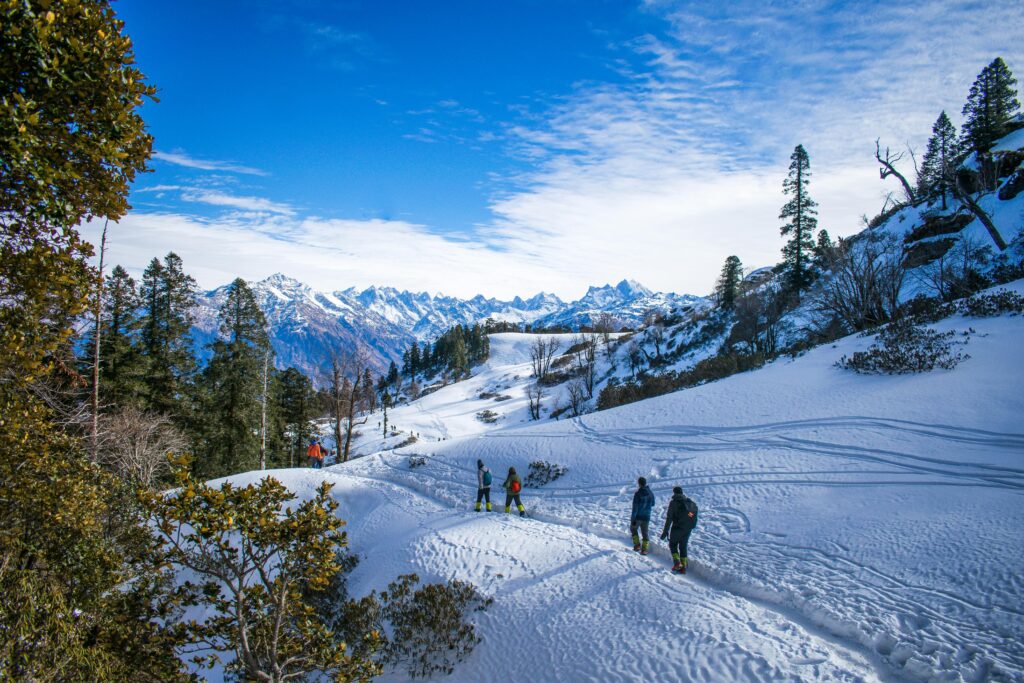 Group of hikers trekking through snowy Himalayan landscape under clear blue sky.