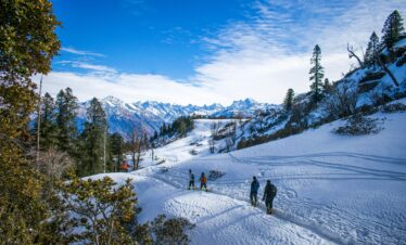 Group of hikers trekking through snowy Himalayan landscape under clear blue sky.