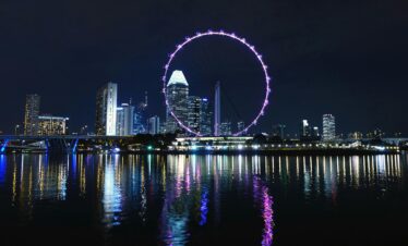 View of Singapore's skyline with the illuminated Singapore Flyer reflecting on Marina Bay at night.