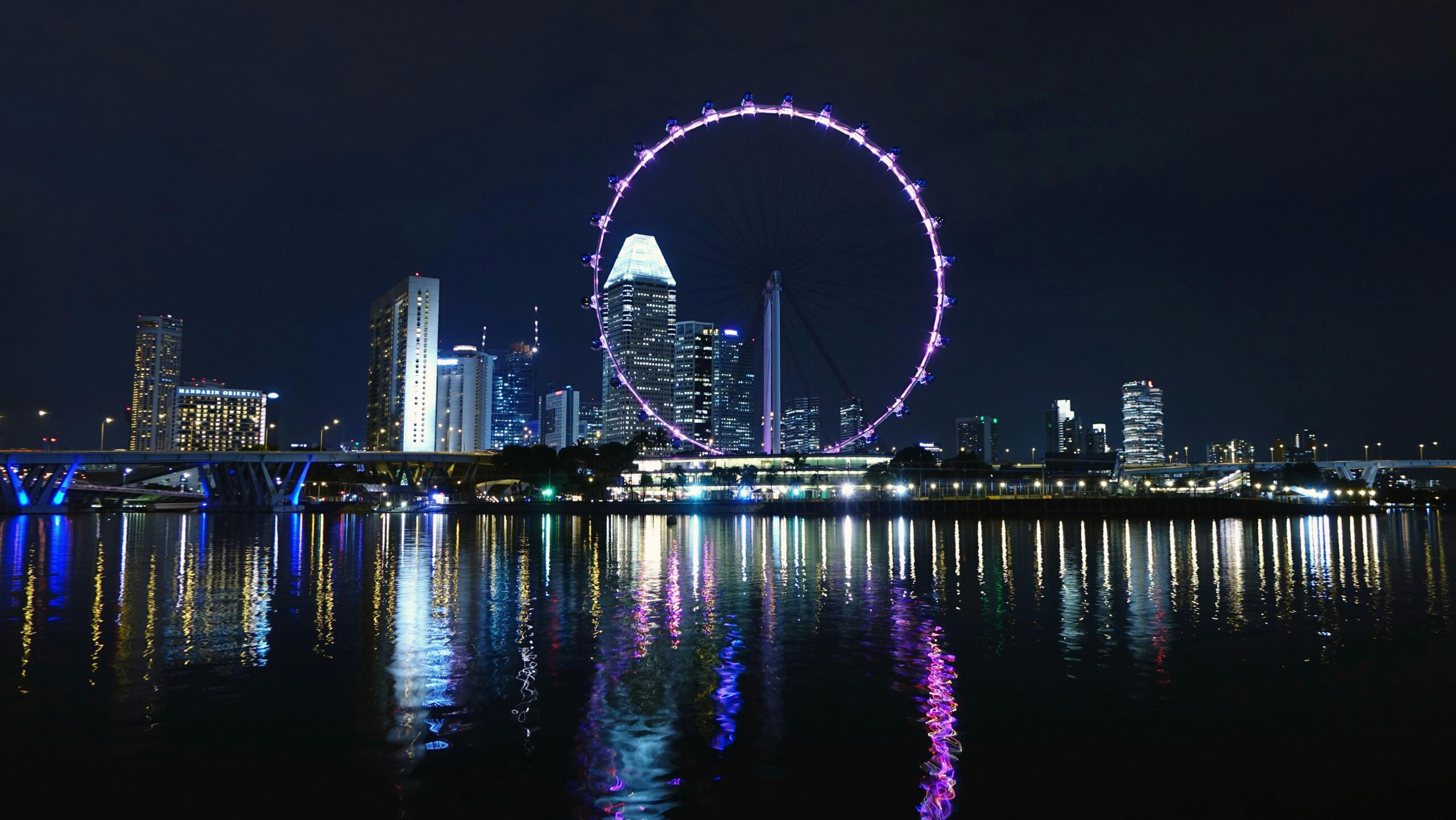 View of Singapore's skyline with the illuminated Singapore Flyer reflecting on Marina Bay at night.